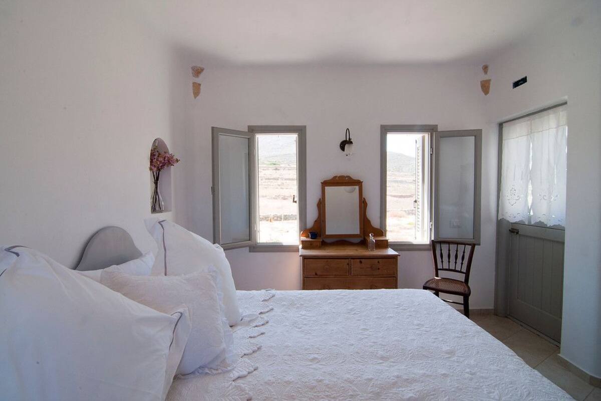 A bedroom with a bed, a dresser, a chair, and two windows.
