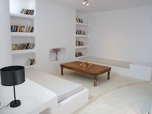 A minimalist living room with white walls, built-in bookshelves, a wooden coffee table, a white sofa, and a black floor lamp.