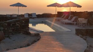 A pool area with lounge chairs and umbrellas, set against a sunset backdrop. - Lithia Villas (Folegandros)