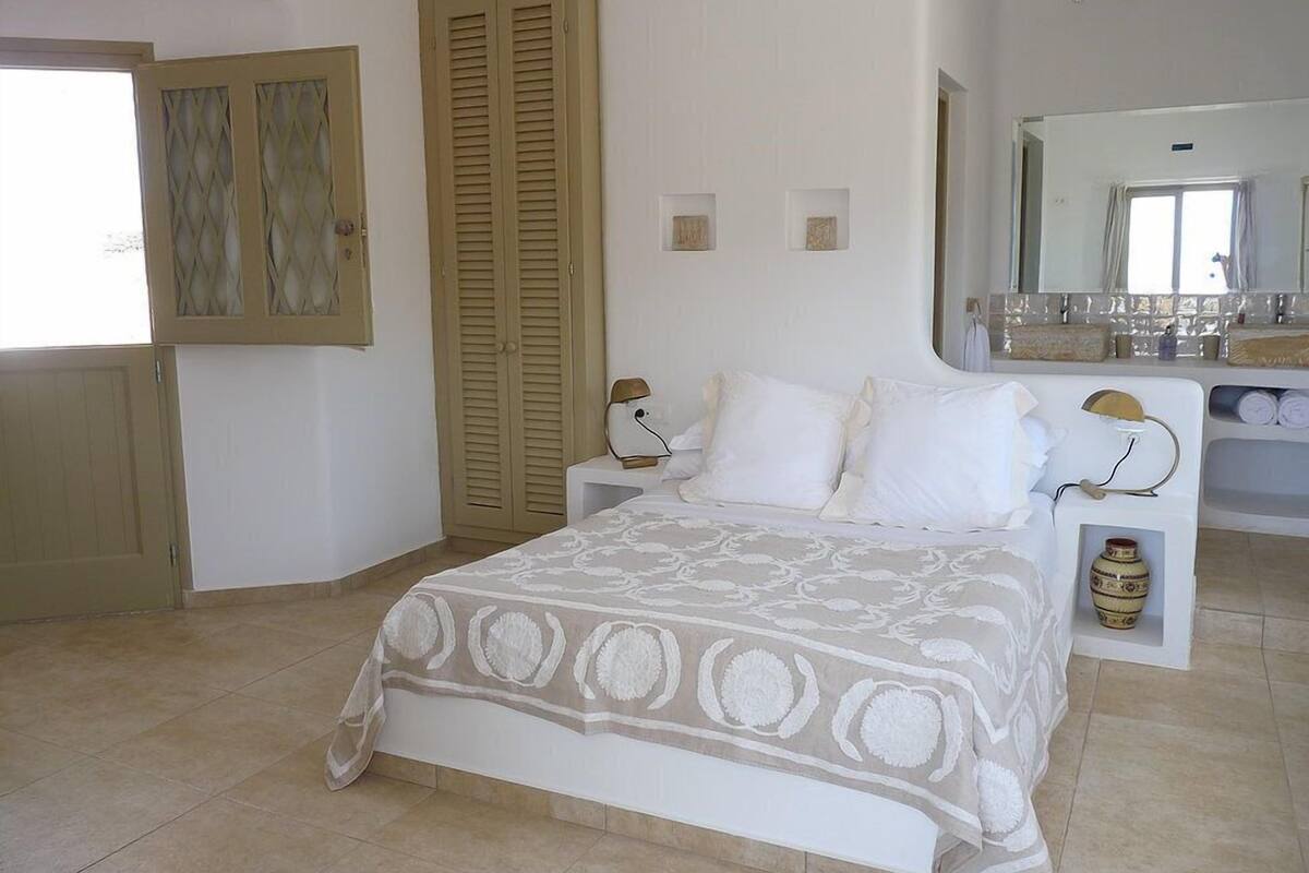 A bedroom with a bed, a wardrobe, a mirror, and a small shelf with toiletries.