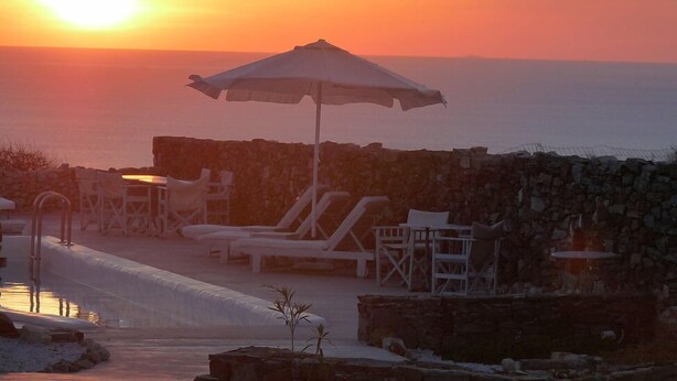 A sunset view from a seaside resort with lounge chairs and an umbrella. - Lithia Villas (Folegandros)