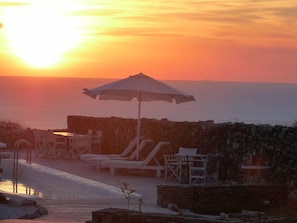 A sunset view from a seaside resort with lounge chairs and an umbrella.