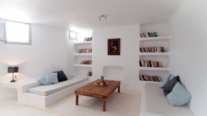 A modern living room with a white sofa, a wooden coffee table, and built-in bookshelves. - Lithia Villas (Folegandros)