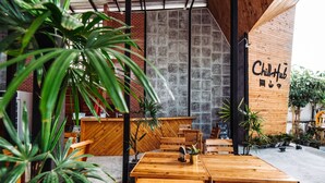 An outdoor seating area with wooden tables and chairs, surrounded by potted plants and a brick wall. - ChillHub Hostel (Choeng Thale)
