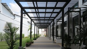 A covered walkway with a metal frame and glass panels, flanked by potted plants and a grassy area. - ChillHub Hostel (Choeng Thale)