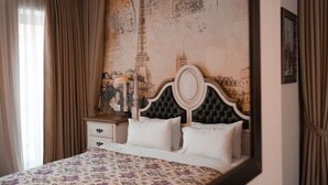 Ein Bett mit floralem Überwurf, ein Nachttisch aus Holz mit einer Lampe und eine Wand mit einem Stadtbild-Fresko.