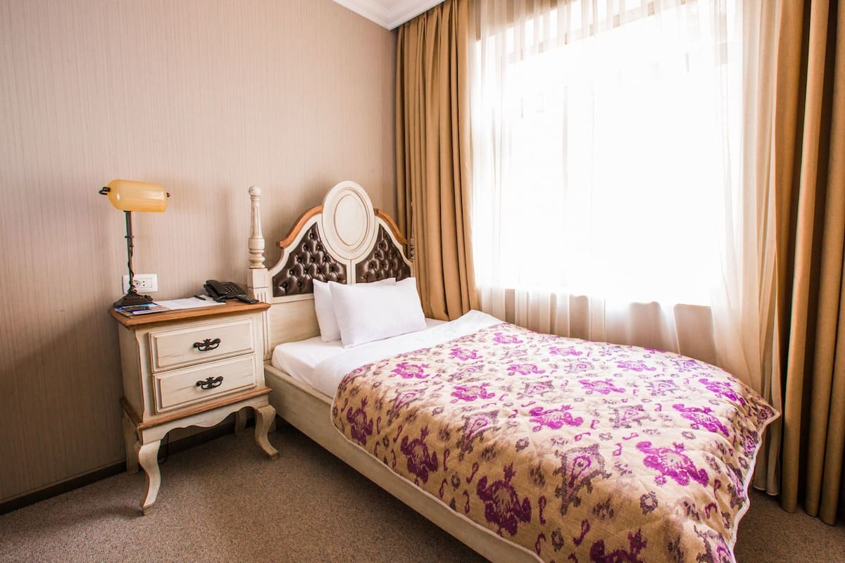 Une chambre d’hôtel avec un lit, une table de chevet avec une lampe, un téléphone et une fenêtre avec des rideaux.