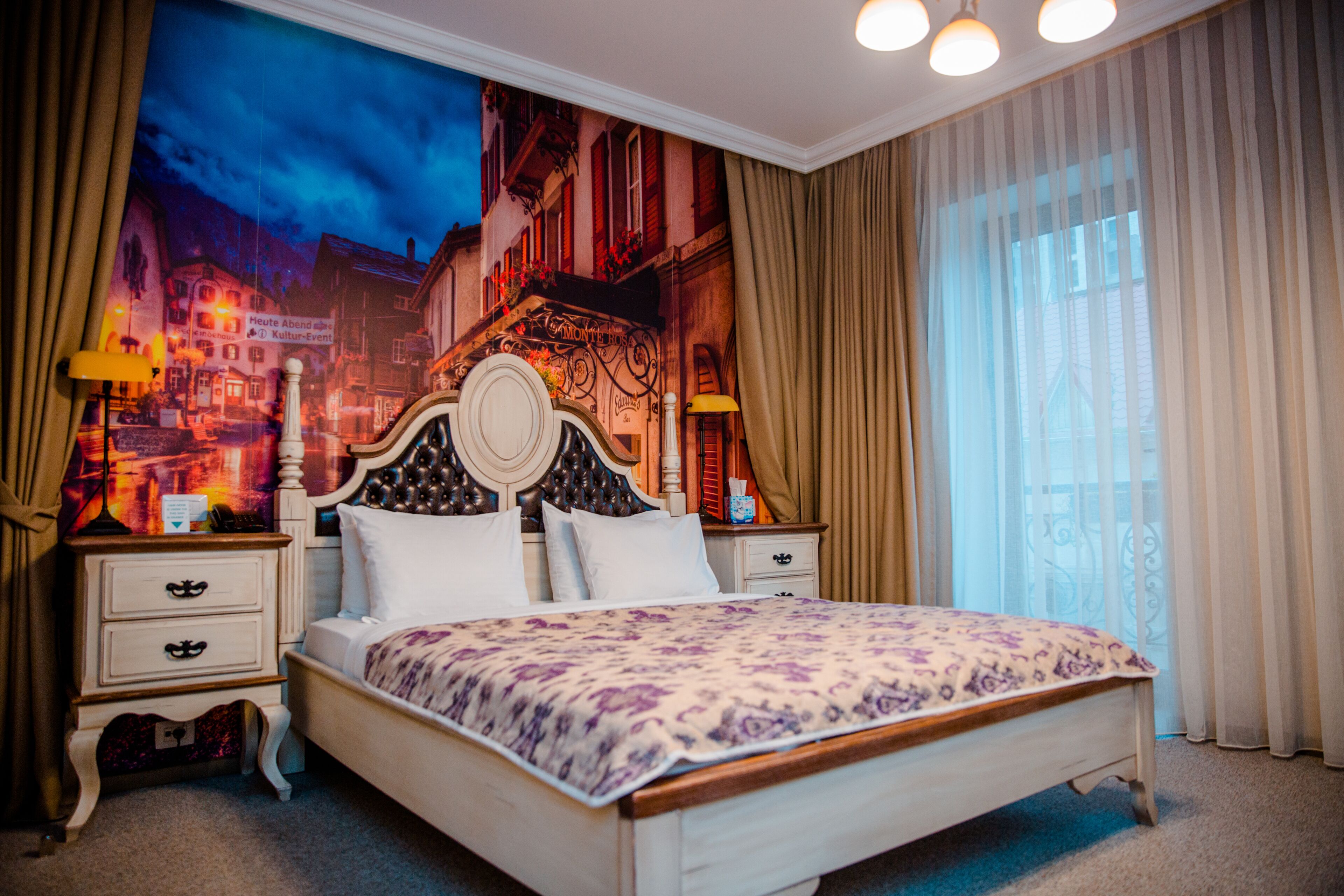 A hotel room with a large bed, two bedside tables, a headboard, and a mural of a cityscape on the wall.