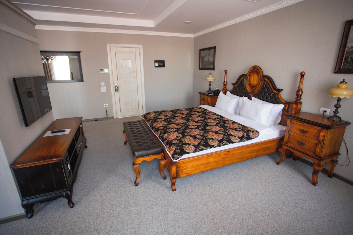 Une chambre à coucher avec un grand lit, un banc en bois, une commode et une table de chevet avec une lampe.