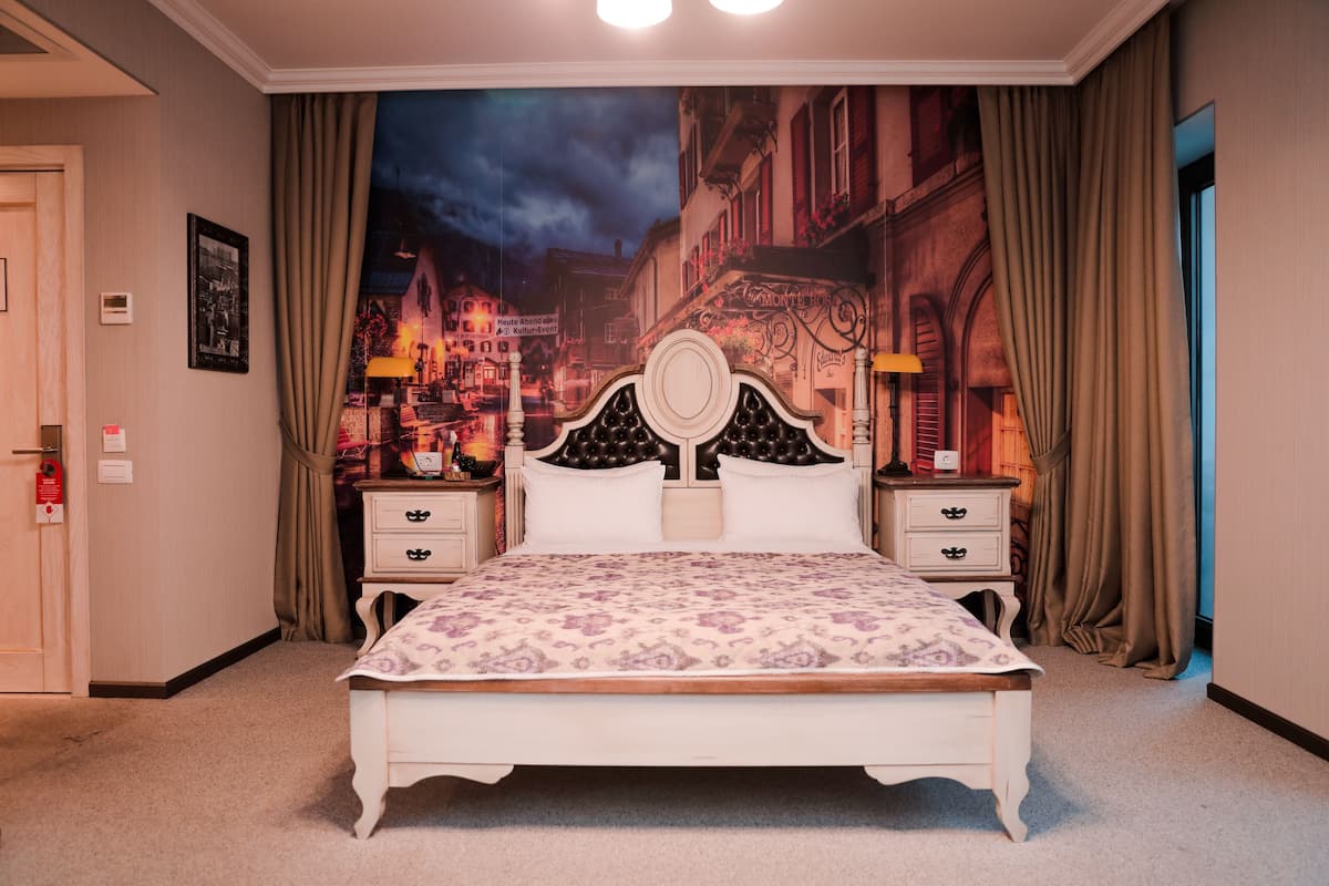 Une chambre à coucher avec un grand lit, deux tables de chevet, une tête de lit et une fresque murale représentant une rue de la ville.