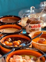 Diverse gerechten in traditionele terracotta potten, waaronder een potje Nutella en honing.