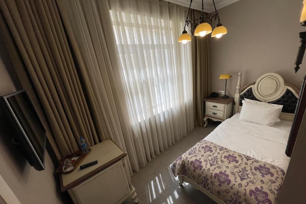 Une chambre d’hôtel avec un lit, une table de chevet, une lampe, une télévision et une fenêtre avec des rideaux.