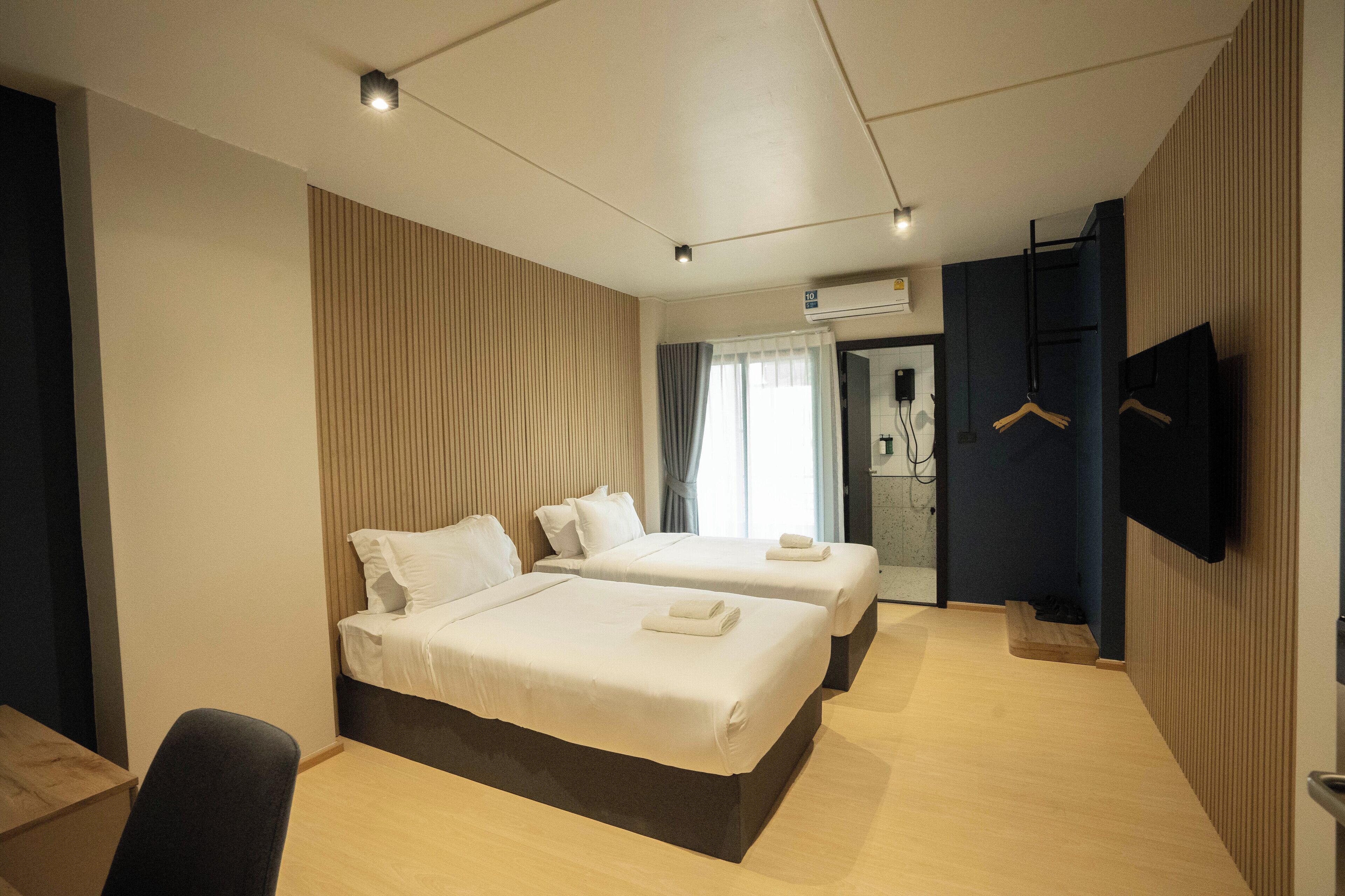 A modern hotel room with two beds, a desk, a chair, a TV, and a wardrobe.