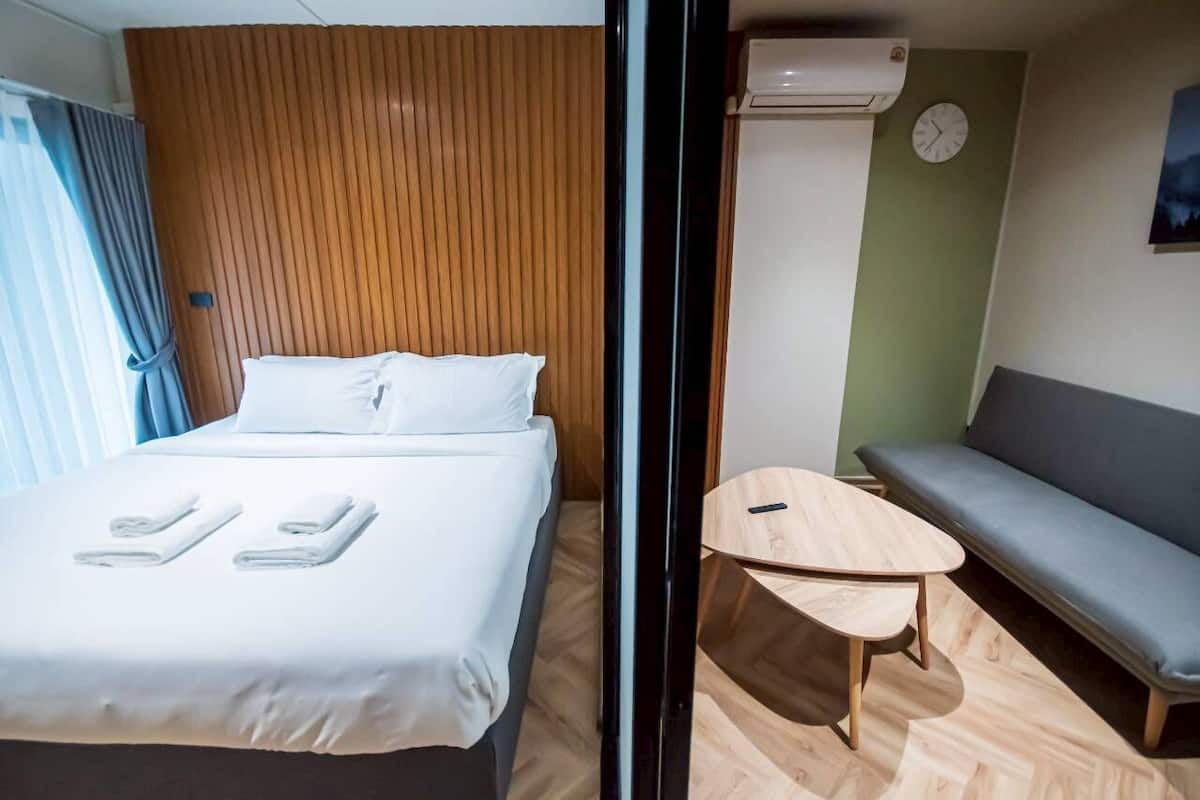 A hotel room with a bed, a small table, a sofa, and an air conditioning unit.