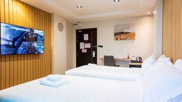 A hotel room with two beds, a desk, a chair, a flat-screen TV mounted on the wall, and a painting on the wall.