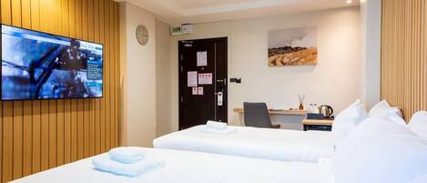 Ein Hotelzimmer mit zwei Betten, einem Schreibtisch, einem Stuhl, einem an der Wand montierten Flachbildfernseher und einem Wandbild.