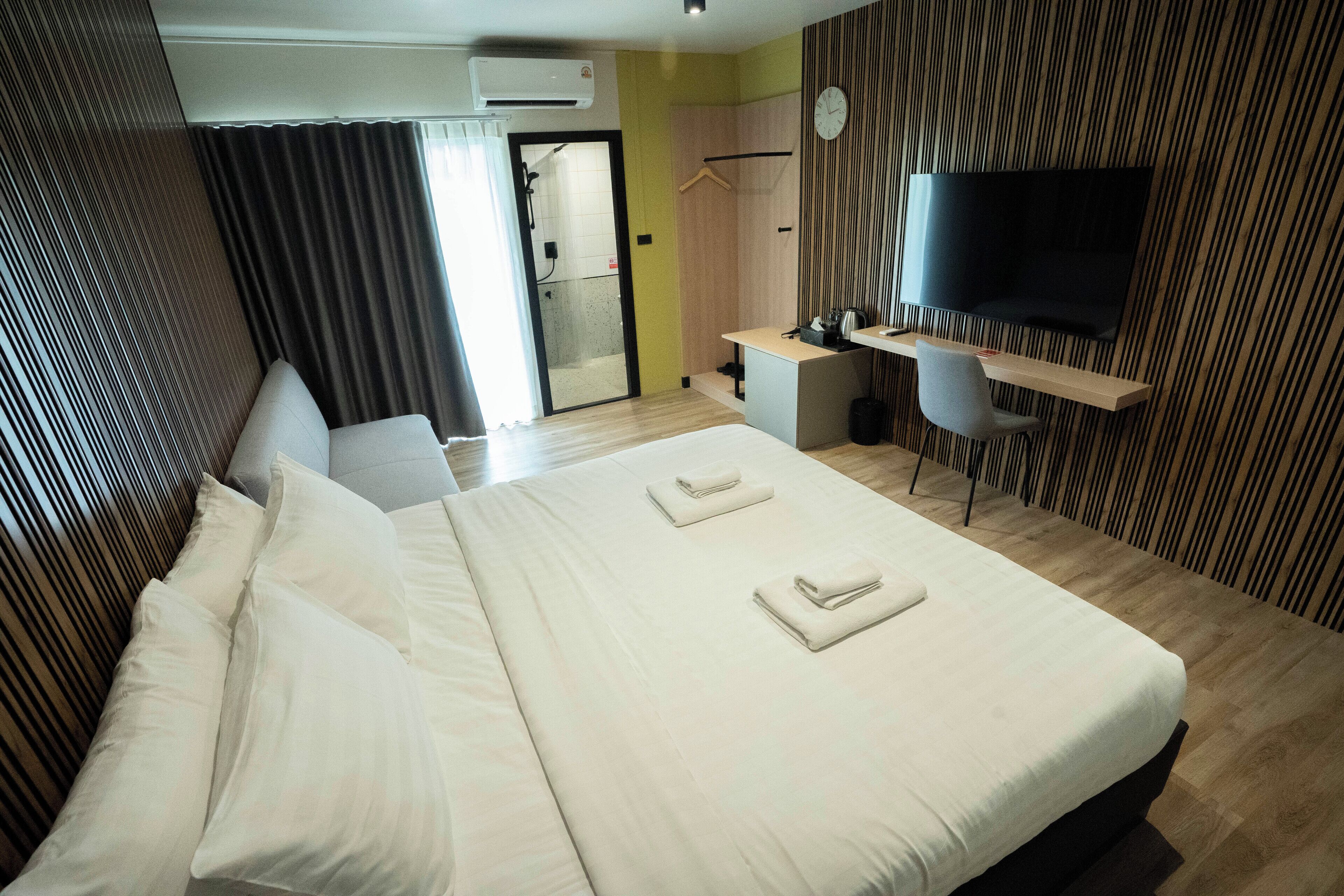 A hotel room with a large bed, a desk with a chair, a TV mounted on the wall, and a shower area.