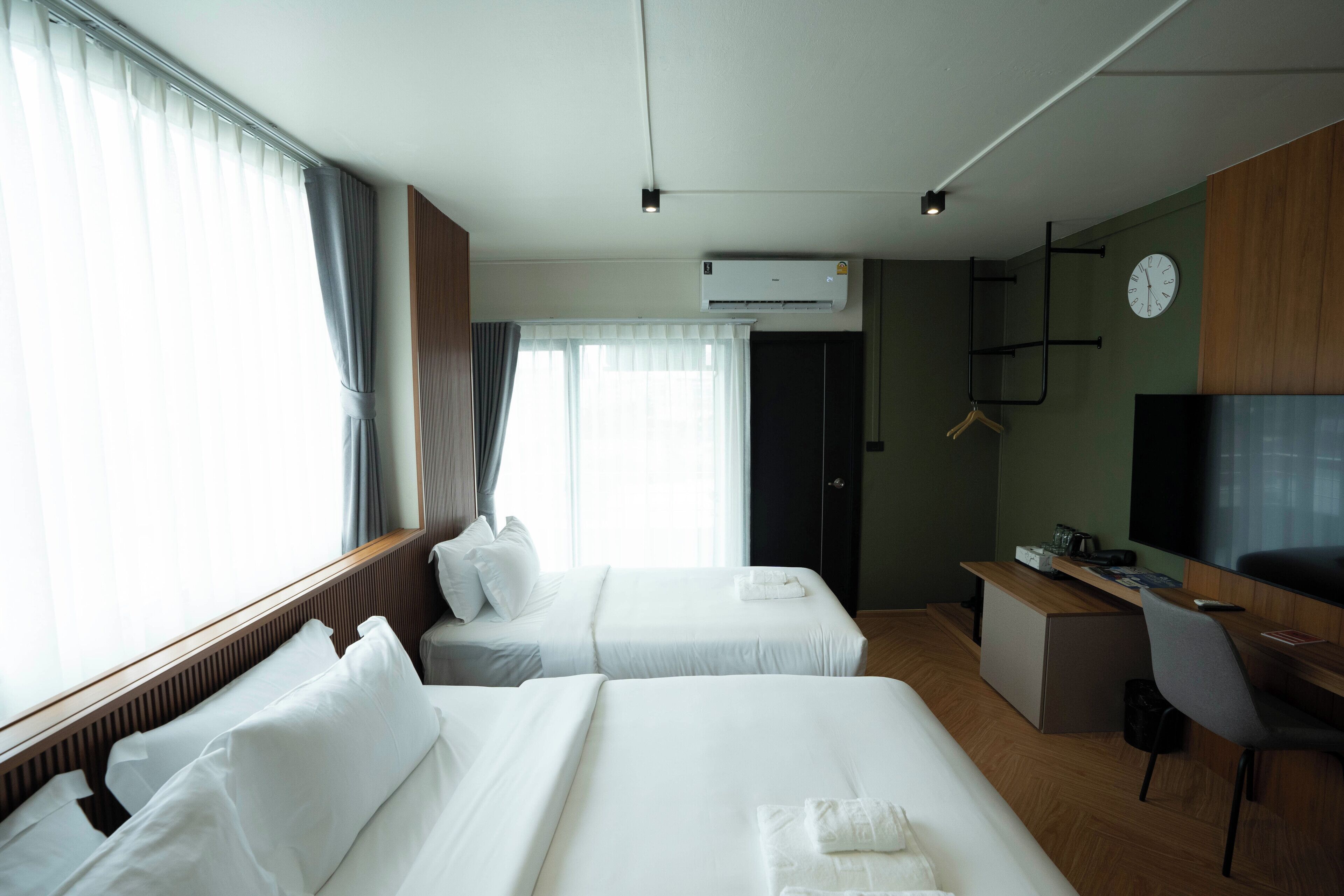 A hotel room with two beds, a desk, a chair, an air conditioner, and a television.