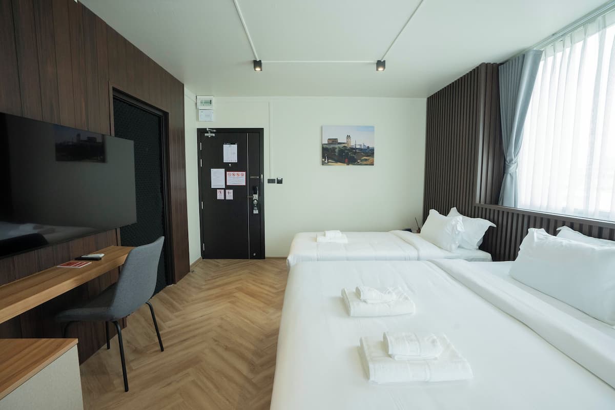 A hotel room with a wooden desk, a flat-screen TV, a bed with white linens, and a large window with curtains.