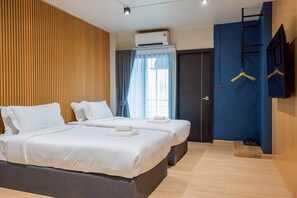 A hotel room with two beds, a wooden panel wall, an air conditioning unit, a door with a blue curtain, and a TV mounted on the wall. - Infinite Hotel at Ratchada (Bangkok)