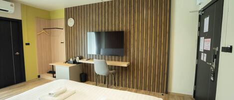A hotel room with a bed, a desk, a chair, a TV, and a wardrobe.