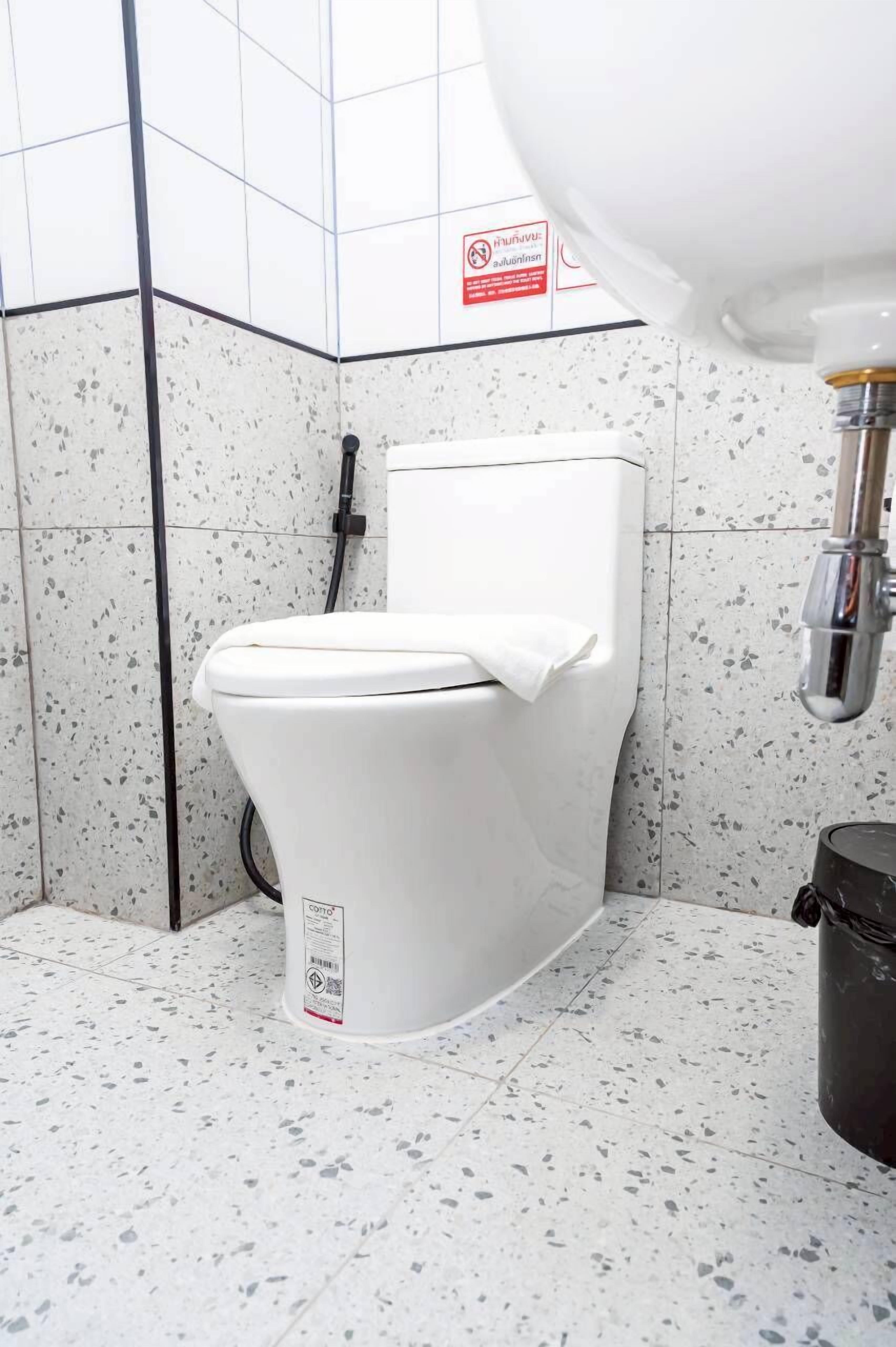 A white toilet with a control panel, a black trash bin, and a water pipe in a tiled bathroom.