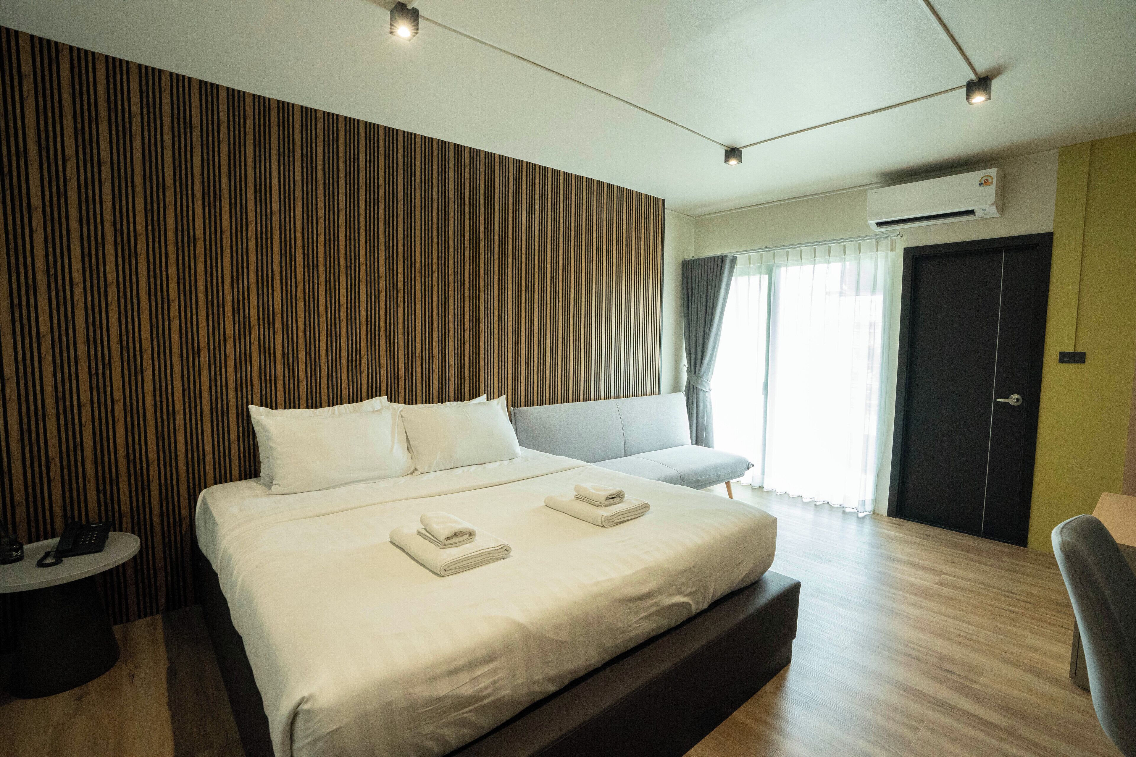 Una habitación de hotel moderna con una cama grande, una mesita de noche con teléfono, un sofá y una puerta con cortina.
