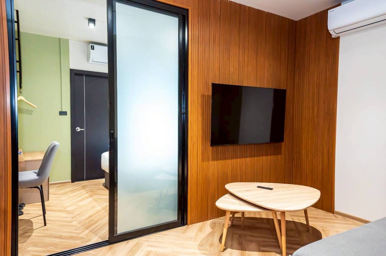 A modern room with a sliding glass door leading to a bathroom, a mounted TV, and a small wooden table.