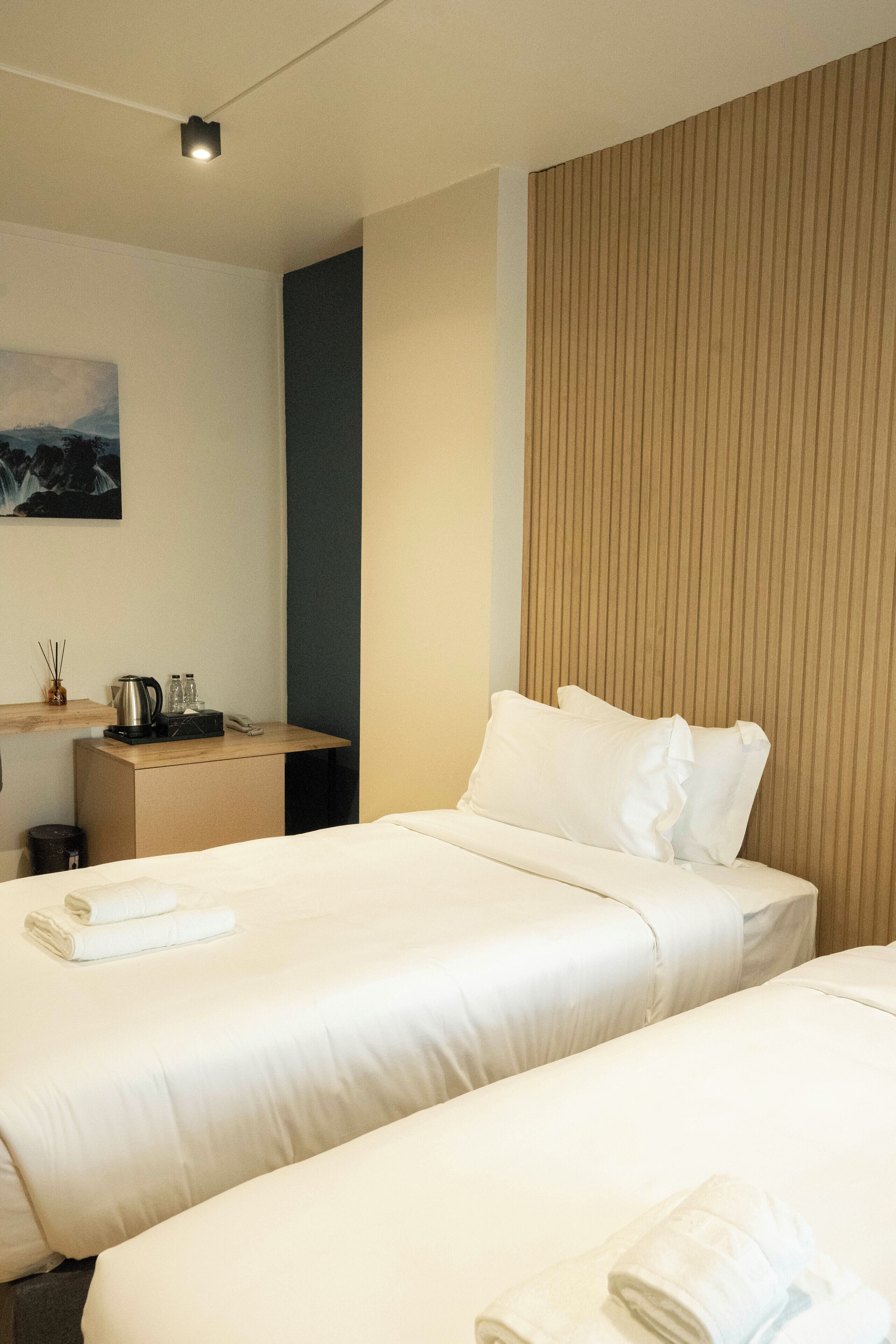 A hotel room with two beds, a desk, and a wall-mounted shelf with a kettle and glasses.