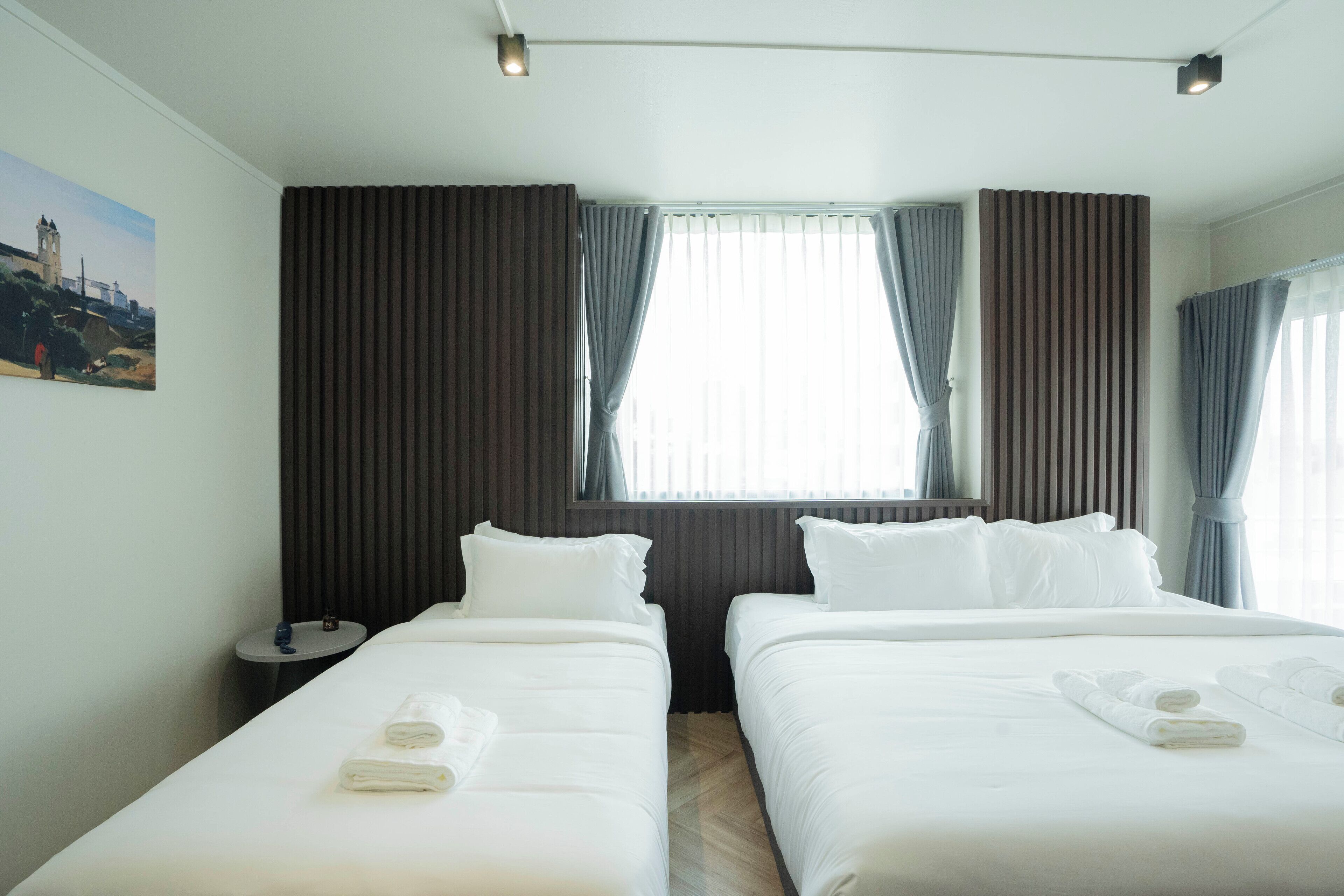 A hotel room with two beds, a nightstand, and a window with curtains.