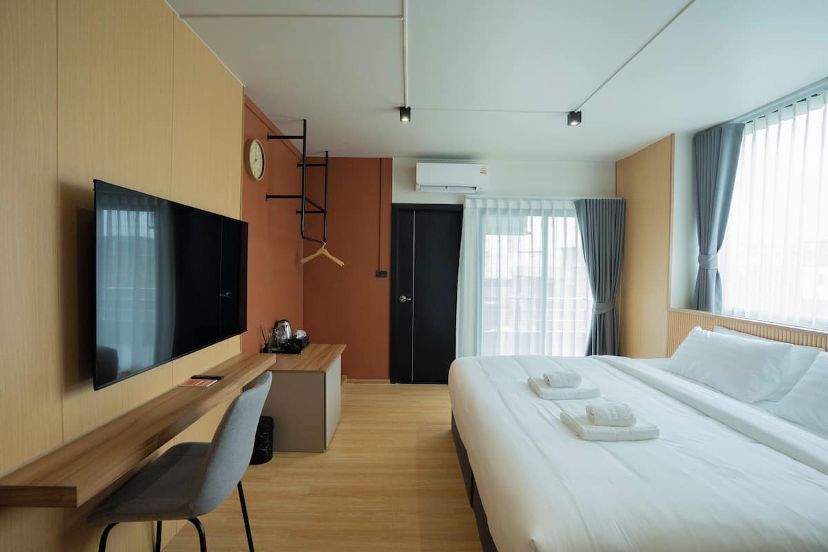 A hotel room with a bed, a desk with a chair, a TV, a wardrobe, and a window with curtains.