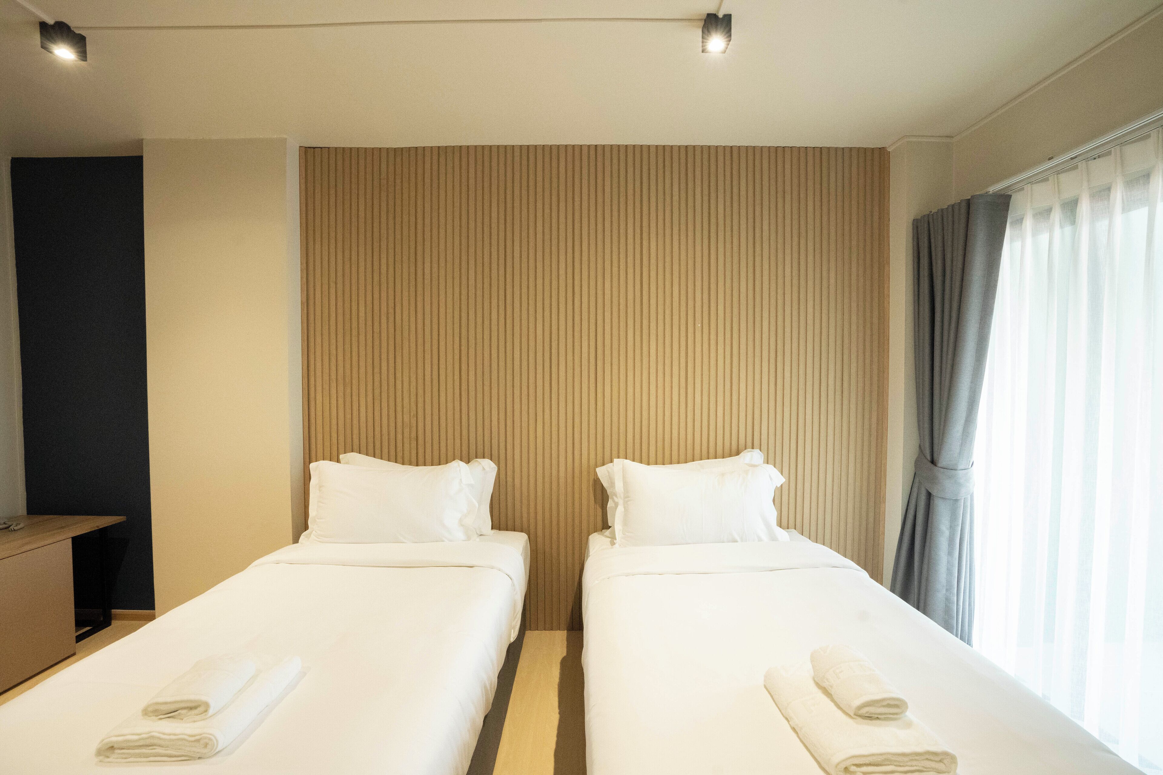 A hotel room with two single beds, a wooden headboard, a desk, and a window with curtains.