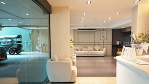 En modern hotellobby med en receptionsdisk, en sittgrupp och en glasvägg med utsikt över ett parkerat fordon utanför.
