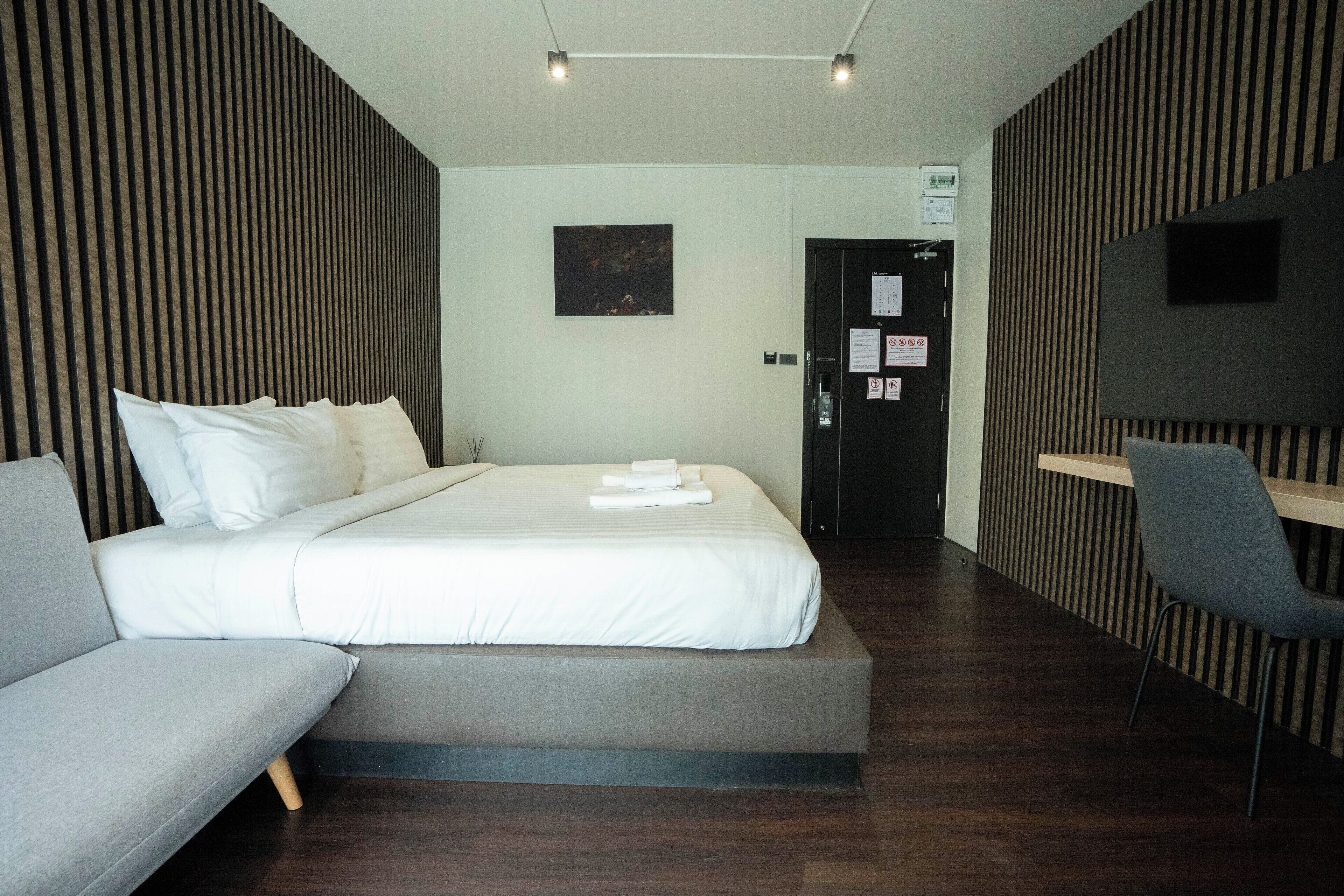 A modern hotel room with a large bed, a sofa, a desk, and a TV.