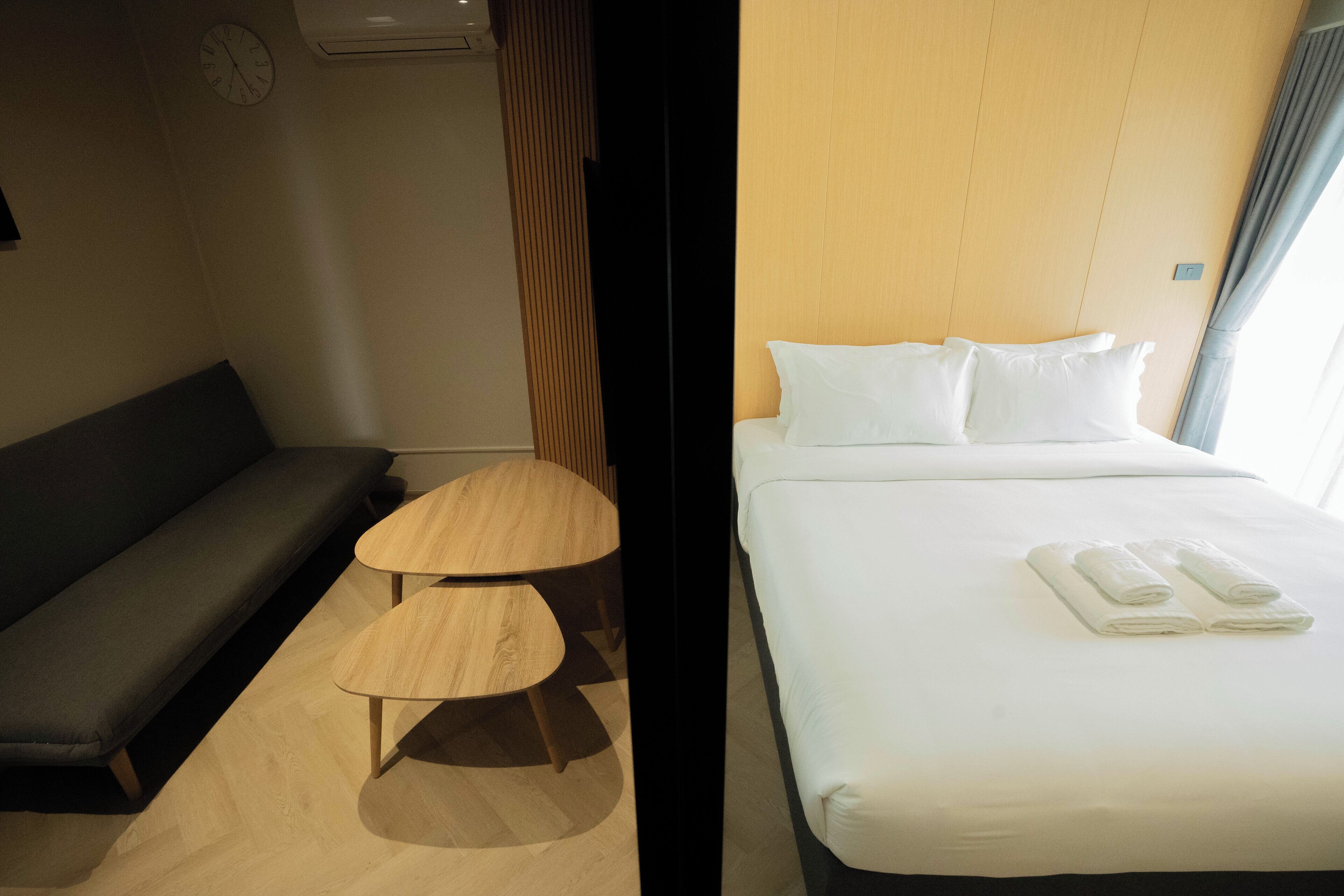 A hotel room with a bed, a sofa, a small wooden table, and a clock on the wall.