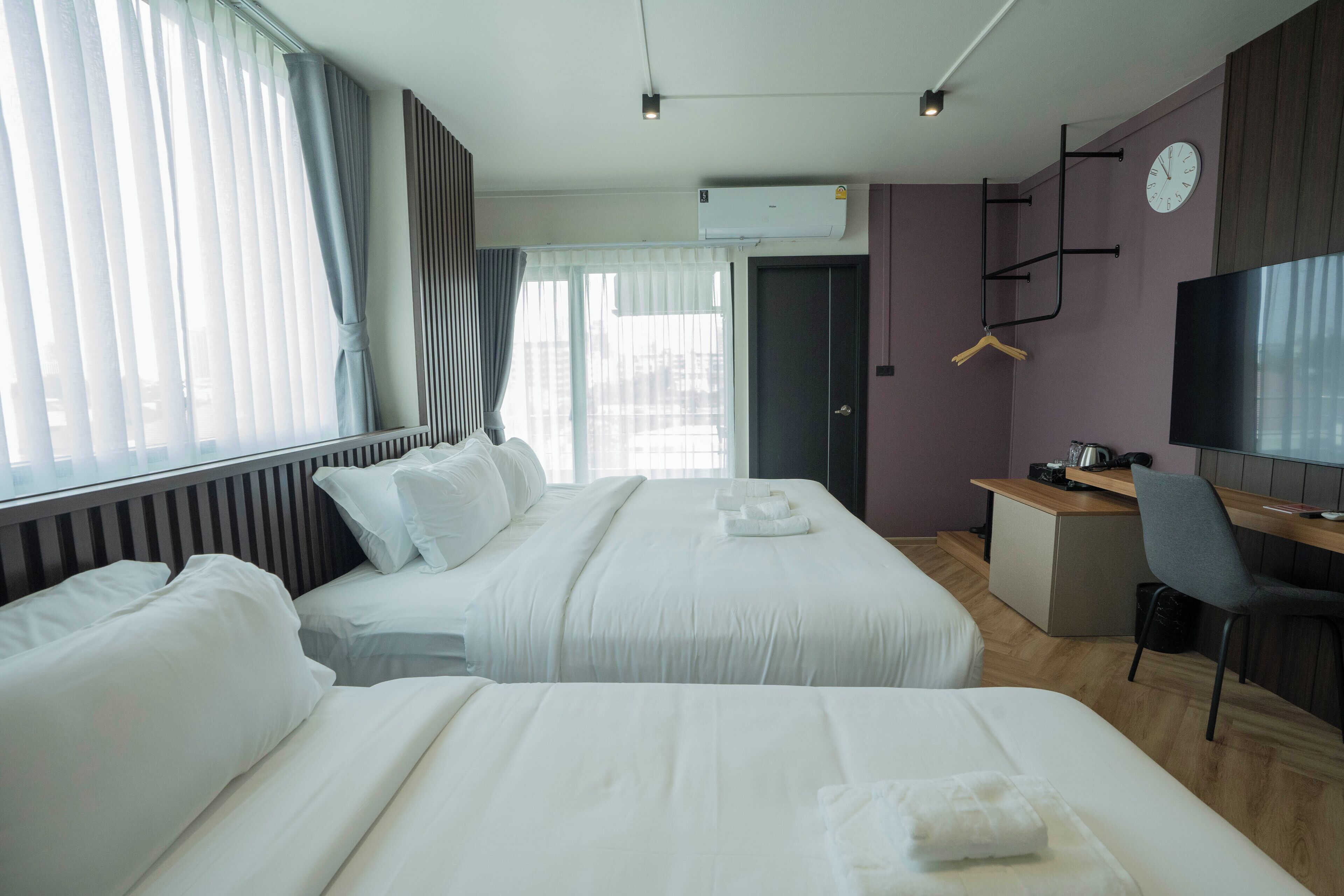 Habitació d'hotel amb dos llits, un escriptori, una cadira, un televisor i un rellotge a la paret.