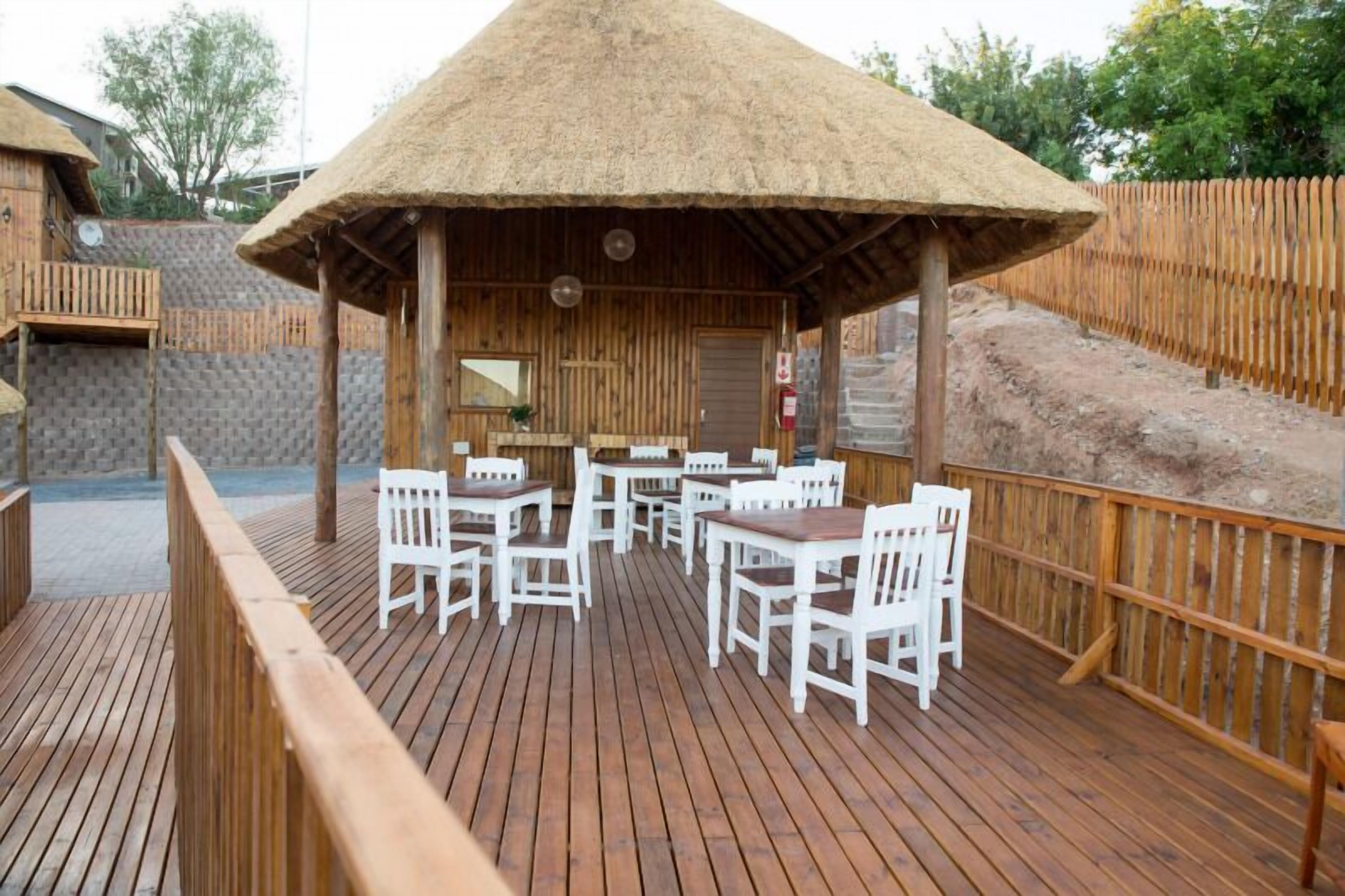 Una terraza de madera con sillas blancas y una estructura de techo de paja.