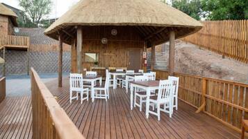 Una terraza de madera con sillas blancas y una estructura de techo de paja.