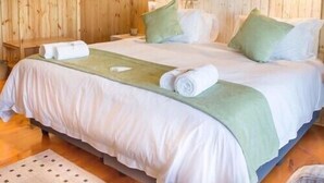 A wooden-paneled room with a bed, pillows, a bedside table, and an air conditioning unit. - Kalahari Lion's Rest (Upington)