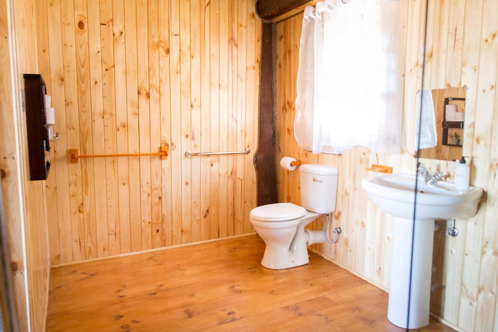 Une salle de bain aux murs lambrissés, équipée de toilettes, d’un lavabo et d’un rideau de douche.