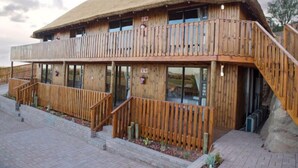 A wooden building with a thatched roof, wooden balconies, and a staircase leading to the entrance. - Kalahari Lion's Rest (Upington)