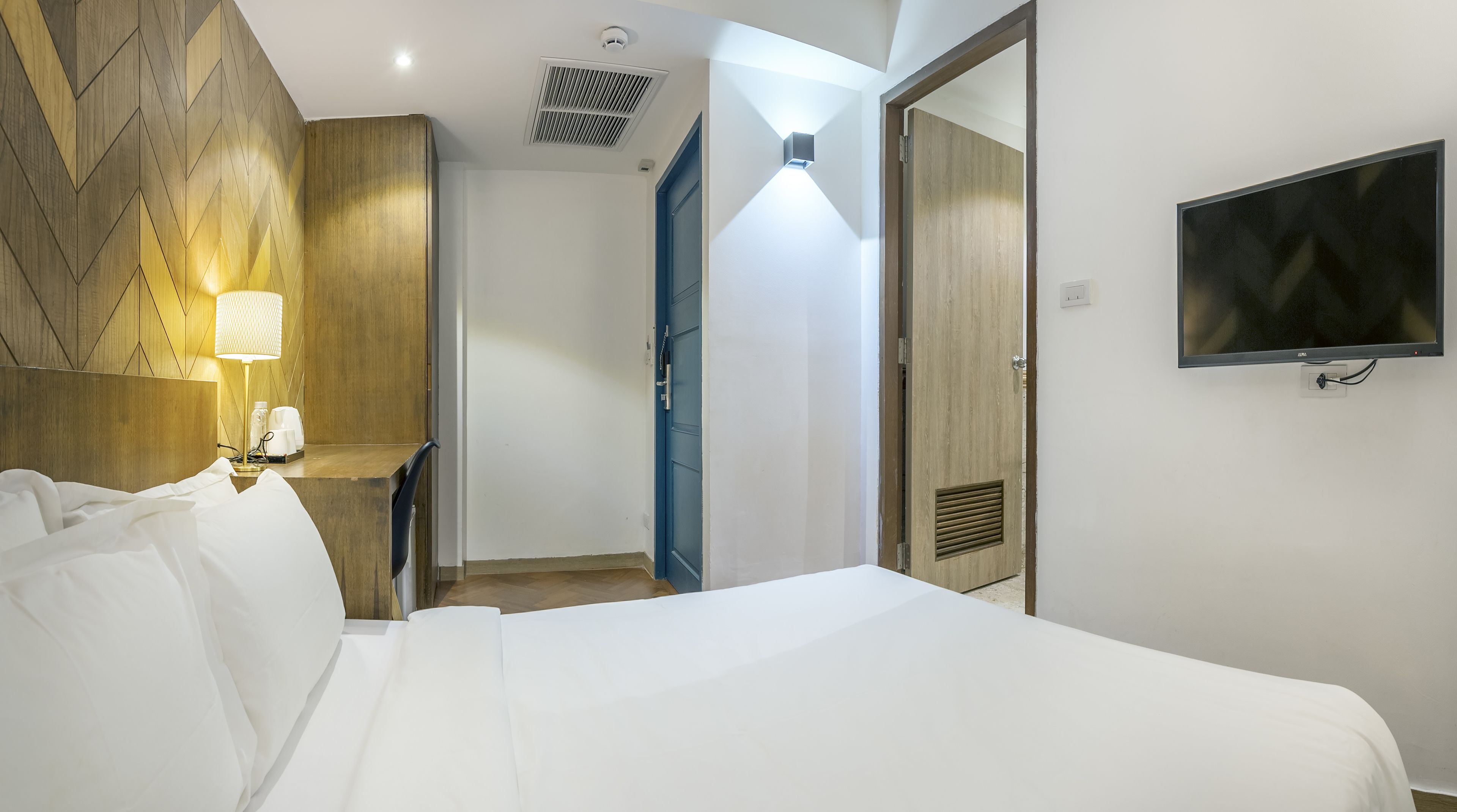 A hotel room with a bed, bedside lamps, a TV, and a wooden accent wall.