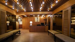 A reception area with a wooden reception desk, two benches, and a large mirror. - THE Posh Phayathai (Bangkok)