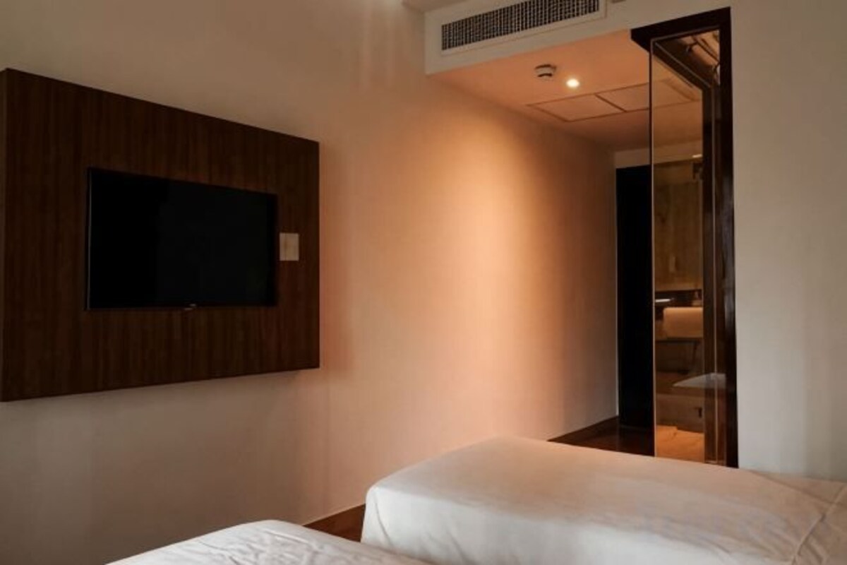 A hotel room with a bed, a television mounted on the wall, and a mirror in the adjacent room.