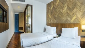 A hotel room with two beds, a wooden herringbone-patterned wall, a TV mounted on the wall, and a nightstand with a lamp. - THE Posh Phayathai (Bangkok)