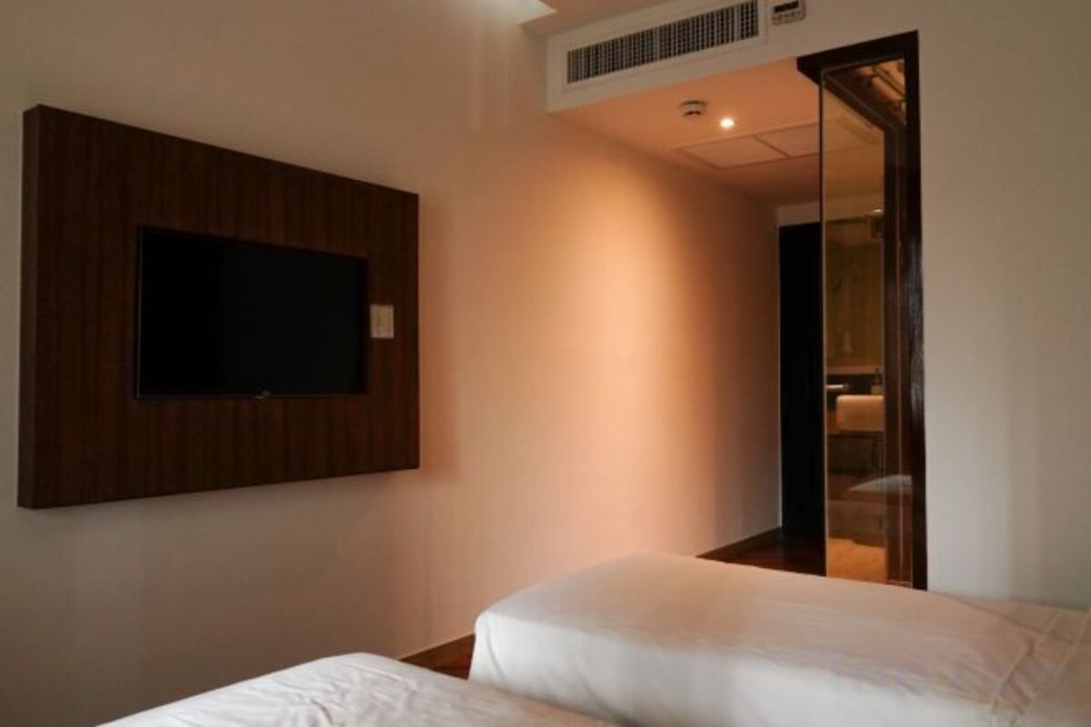 Quarto de hotel com cama, televisão montada e porta deslizante para um banheiro.