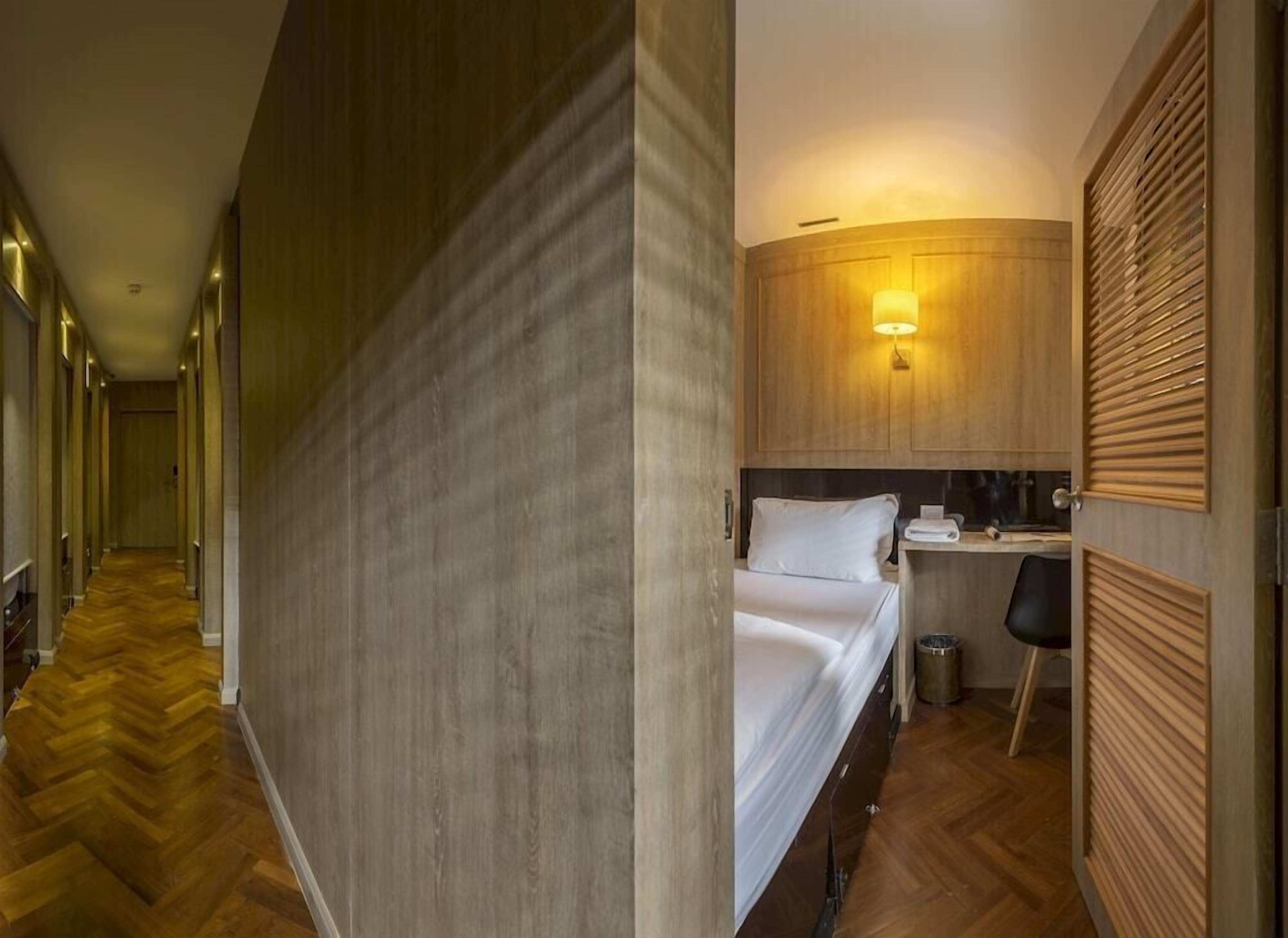 Een hotelkamer met een bed, een bureau, een stoel, een lamp en een houten vloer.