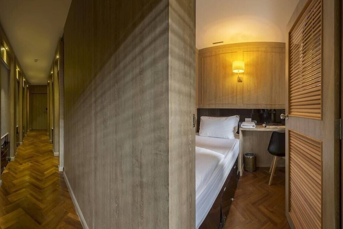 Une chambre d’hôtel avec un lit, un bureau, une chaise, une lampe et un plancher en bois.