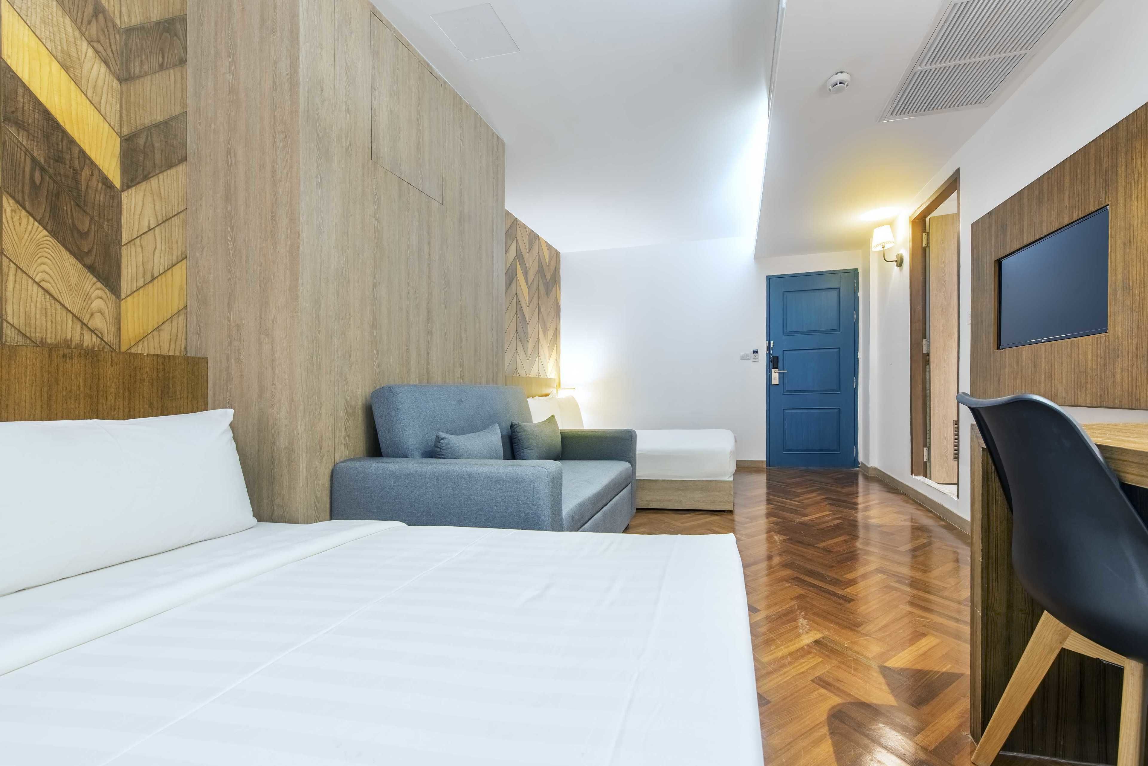 A modern hotel room with a large bed, a sofa, a desk, and a TV.