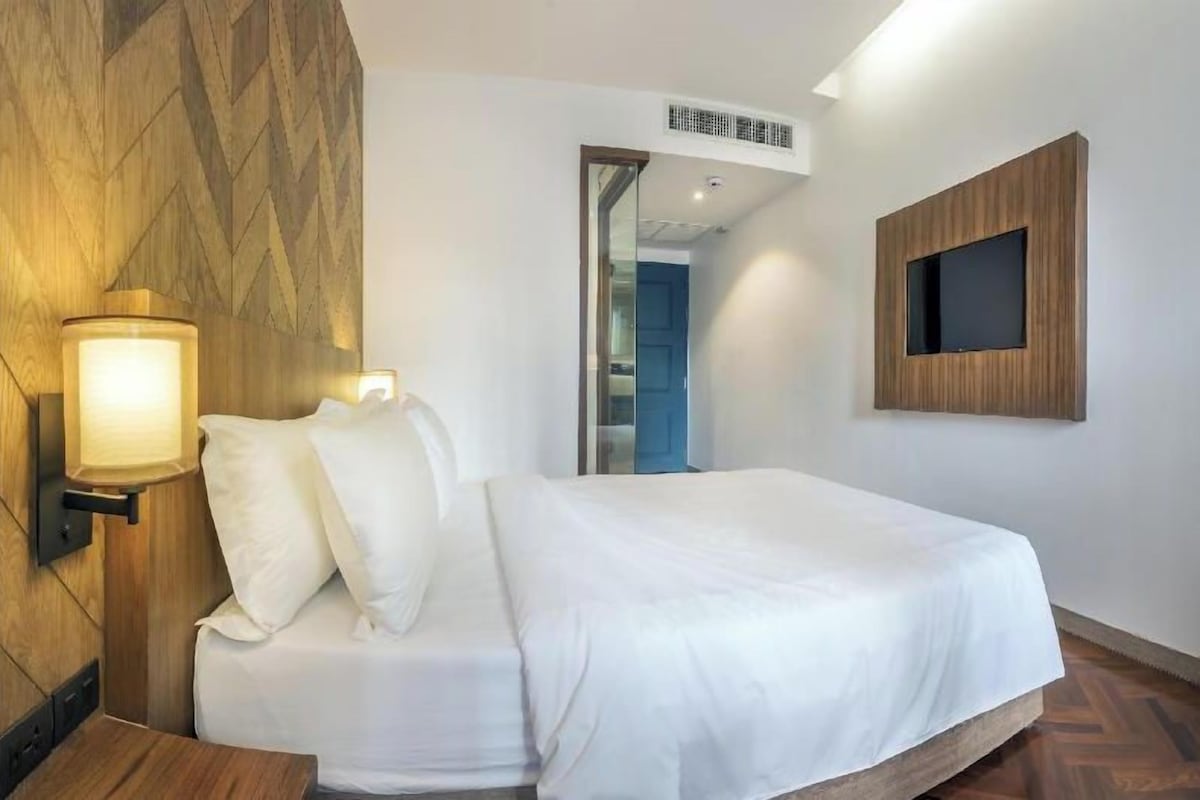 A hotel room with a bed, a wall-mounted TV, and a wooden accent wall.
